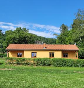 a yellow house with a green field and trees at Chaty u Tesaru in Bítov