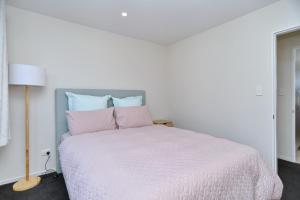 Dormitorio blanco con cama blanca y almohadas rosas en Thomas Townhouse - Christchurch Holiday Homes en Christchurch