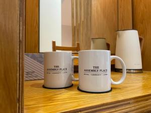 dos tazas de café blancas sentadas en un estante en The Assembly Place, A Co-living at Mayo en Singapur
