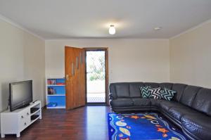 a living room with a black leather couch and a television at Alwyns By The Sea - Free Wi-Fi and Pet Friendly Outside Only in Inverloch