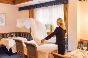 a woman is setting a table in a restaurant at Wellness Refugium & Resort Hotel Alpin Royal - Small Luxury Hotels of the World in Cadipietra