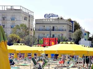 リミニにあるHotel Cobaltoの黄色のパラソルと椅子が並ぶビーチと建物