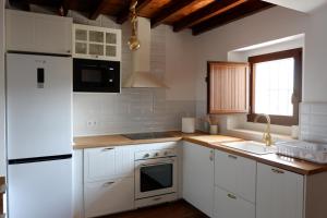 cocina con armarios blancos y nevera blanca en CASA HESTIA, en Arriondas