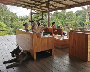 a group of people sitting on benches on a deck with a dog at Hotel Finca Maresia in Drake