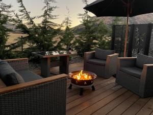 eine Feuerstelle auf einer Terrasse mit Stühlen und einem Sonnenschirm in der Unterkunft Orchard Lodge Wanaka - Relax, Refresh, Recharge in Wanaka