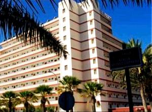 un grande edificio bianco con palme di fronte di ELDORADO 2 BEDROOMS a Playa de las Americas