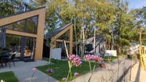 ein Haus mit Glastüren und lila Blumen im Hof in der Unterkunft Village Mielno - najpiękniejsze domki wakacyjne nad morzem in Mielno