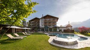 een resort met een zwembad en stoelen en een gebouw bij Hotel Burggräflerhof in Merano