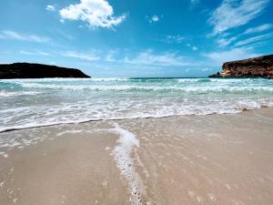 una spiaggia sabbiosa con onde nell'oceano di Appartamento con giardino a Lampedusa