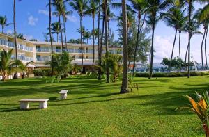 a park with benches and palm trees in front of a building at Résidence Hôtelière Le Carayou in Les Trois-Îlets