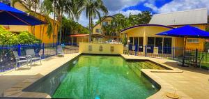 ein Pool mit blauen Sonnenschirmen neben einem Haus in der Unterkunft Rainbow Beach Dream Studio Motel Style Apartment in Rainbow Beach
