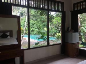 1 dormitorio con vistas a la piscina a través de las ventanas en Raka Rai Bungalows, en Ubud