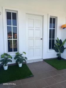 una porta bianca con due piante in vaso davanti di Safiyya Homestay a Pantai Cenang