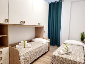 2 Betten in einem Zimmer mit weißen Schränken und grünen Vorhängen in der Unterkunft Itaca in Lido di Fermo