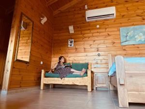 Aviv - Bakfar in Amirim في أمريم: امرأة تجلس على سرير في غرفة خشبية