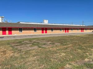 a large building with red doors and a grass field at Vento Hotel in Hutchinson