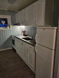 La cuisine est équipée de placards blancs et d'un réfrigérateur blanc. dans l'établissement Off-the-grid cabin on the island of Senja in northern Norway, à Brygghaugen