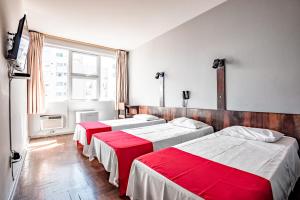 a room with three beds and a tv and a window at Cannes Palace Hotel in Vitória