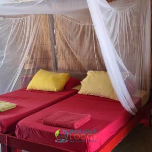 a bed in a tent with red sheets and yellow pillows at Campement Hakuna Lodge in Mar Lodj