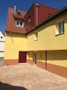 un grand bâtiment jaune avec un toit rouge dans l'établissement Gite du Meunier, à Voegtlinshoffen