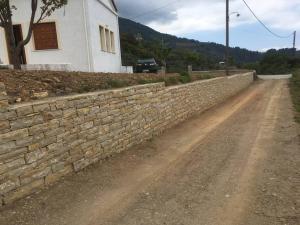 a stone wall on a dirt road next to a building at Manolates 360 views sea and mountains in Valeontádes