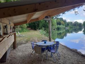 a table and chairs under awning next to a lake at LES GITES DU PARC MANTOCHE LE TONNEAU in Mantoche