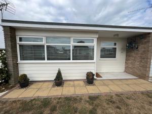 a white house with two potted plants in front of it at Lazy Dayz, Chalet 179, Hemsby - Two bed chalet, sleeps 4, free Wi-Fi, pet free, close to beach in Hemsby
