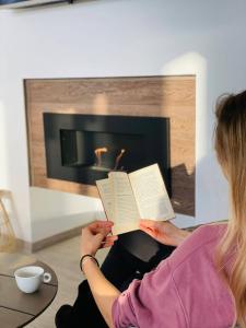 a woman reading a book in front of a fireplace at Cabana Chalet Transylvania in Orlat