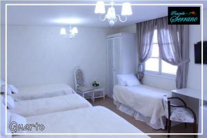 a white bedroom with two beds and a window at Pousada Serrano in Campos do Jordão