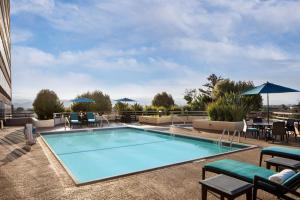 - une piscine avec des chaises, des tables et des parasols dans l'établissement Sonesta San Jose - Milpitas, à Milpitas