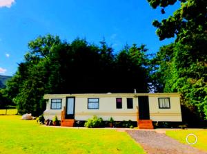 a small caravan in a yard with trees at CAYORETREAT STATIC CARAVAN in Longtown