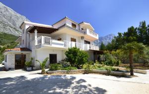 uma grande casa branca com palmeiras e montanhas em Family friendly apartments with a swimming pool Baska Voda, Makarska - 12442 em Baska Voda