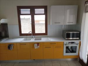 eine Küche mit gelben Schränken, einem Waschbecken und einem Fenster in der Unterkunft Villa saisonnière Montalegre Lamentin in Lamentin