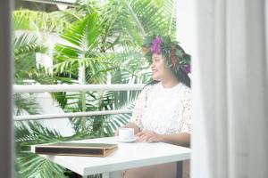 a woman sitting at a table with a book and a cup of coffee at Hotel Beaurivage in Noumea
