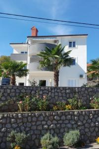 a white building with palm trees behind a stone wall at Apartments with a parking space Kastav, Opatija - 13457 in Kastav
