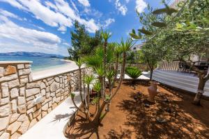 a garden with trees and a stone wall and a beach at Apartment Arbanija 14825b in Trogir