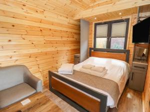 a bedroom with a bed and a chair in a log cabin at The Shepherds Hut at Bridge Lake Farm & Fishery in Banbury