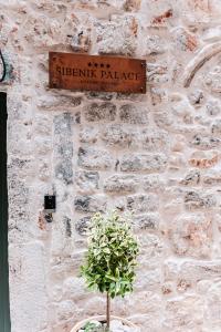ein Schild an einer Ziegelmauer mit einer Pflanze davor in der Unterkunft Šibenik Palace in Šibenik