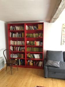 een rode boekenplank gevuld met boeken naast een bank bij Les Rosiers in Eschbourg