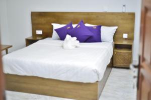 um bicho de peluche branco sentado numa cama com almofadas roxas em Tenda Suites and Restaurant em Entebbe