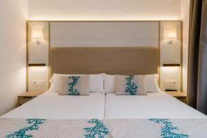 1 dormitorio con 1 cama blanca grande con almohadas en Alua Suites Las Rocas, en Cala d´Or