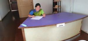 Una donna seduta a un tavolo con un cartello sopra di Mulu Homestay a Mulu