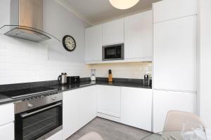 a kitchen with white cabinets and a clock on the wall at PenthouseStays Notting Hill - Chic 2 Bedroom Apartment w/ King Beds - near Portobello Road & Kensington High Street in London
