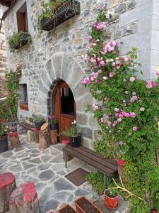 un edificio de piedra con un banco y rosas rosas en Casa rural ELURKOIA en Isaba