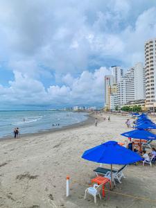 una playa con sombrillas azules y gente en el océano en Hotel Cabreromar By GEH Suites en Cartagena de Indias