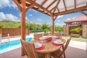 a wooden table and chairs on a patio with a pool at Bungalow Pom 1, piscine, à 5 min des plages in Le Vauclin