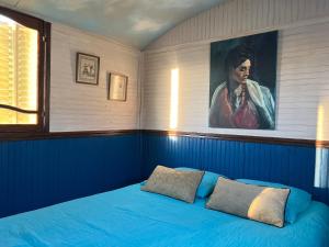 a bedroom with a blue bed with a portrait of a man at La Roulotte Bohème des Grillots in Beaulon