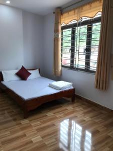 um quarto com uma cama com uma janela e um piso de madeira em Nhà Nghỉ Minh Hảo em Làng Môn