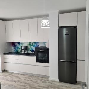 La cuisine est équipée de placards blancs et d'un réfrigérateur noir. dans l'établissement Panoramic Apartment, à Braşov