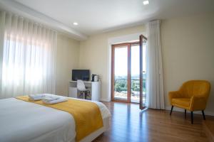 ein Schlafzimmer mit einem Bett, einem Stuhl und einem Fenster in der Unterkunft Villa Tavares Suítes in Arouca